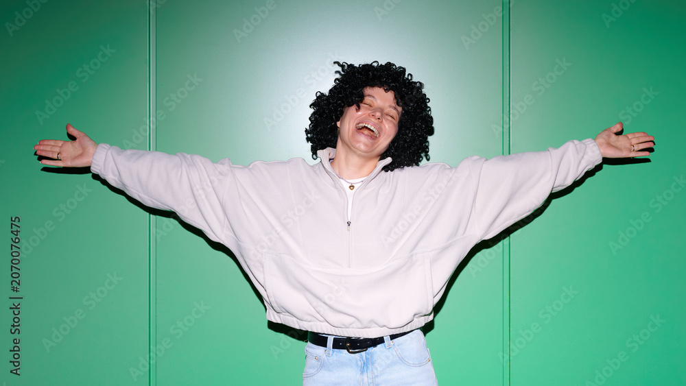Naklejka premium Joyful young woman with curly wig and arms outstretched in a gesture of pure happiness and freedom