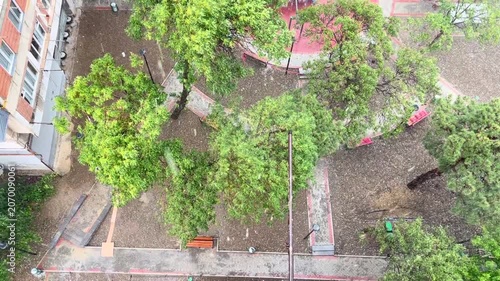 Heavy city rain falling over green trees, rooftops and courtyard during summer storm, viewed from above