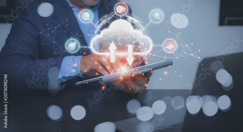A businessman in a suit uses a tablet with a glowing cloud storage icon, with upload and download arrows.