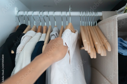A person's hand selecting a white shirt from a neatly organized wardrobe clothes rack.