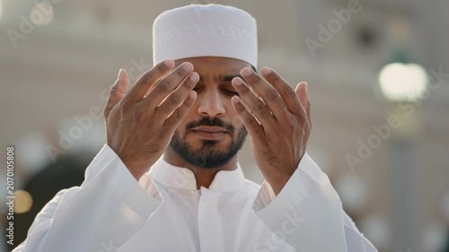 Devoted Muslim man subtly moving open hands in prayer, eyes closed, reflecting spiritual devotion in Makkah