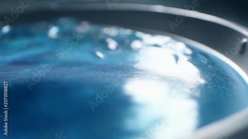 Blue liquid creating abstract ripples and waves on a reflective surface, highlighting movement and dynamic fluid textures in a dark, clean environment