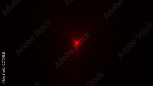 A single bright red circular light flare glowing in the center of a deep black background creating a minimalist abstract visual effect with soft rays