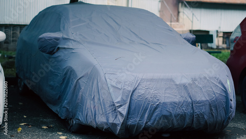 Fotografía A car is parked outdoors while completely covered by a protective grey fabric s