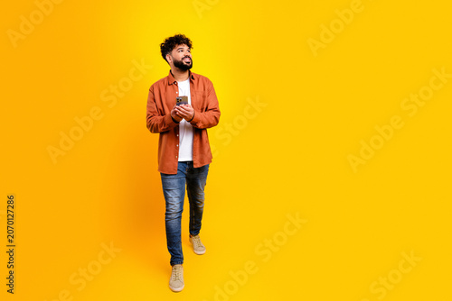Konstfotografi Casual young man in a photo studio with yellow background holding smartphone and