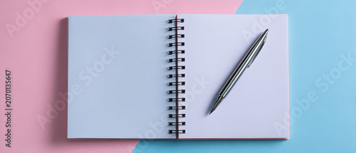 Top view of an open spiral notebook and pen on a pink and blue pastel background, suitable for education, business, or creative concepts.