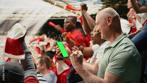 Vertical chroma key phone screen with football fan during soccer match in a packed stadium crowd, Supporters chanting and cheering for the red team, authentic live football match culture.