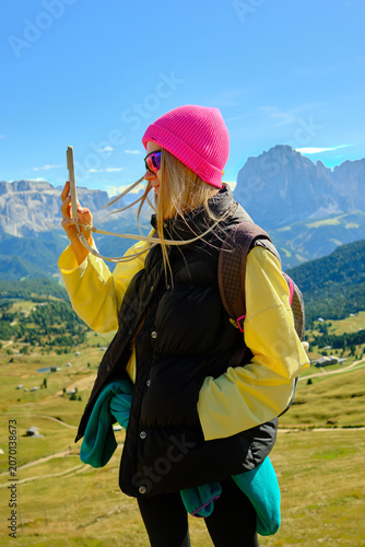 Young woman in bright outfit taking selfie on sunny day in mountains surrounded by nature scenery