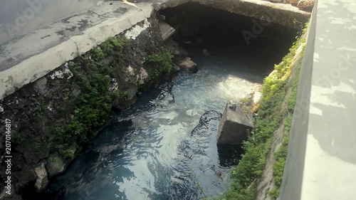 Polluted Concrete Drainage Canal With Stagnant Water And Green Vegetation Growth On Stone Walls
