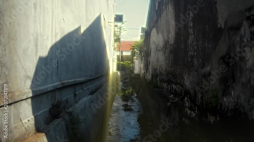 Narrow Urban Drainage Canal Between Aged Concrete Walls With Natural Sunset Sunlight And Lens Flare