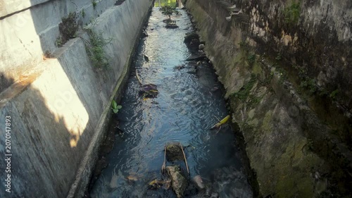 Polluted Concrete Water Canal In Urban Environment With Dark Flowing Water And Debris