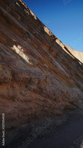 Vertical Screen: Dramatic layered rock formations in Golden Canyon at Death Valley National Park California. Stratified sedimentary cliffs display warm red and brown tones under bright sunlight.