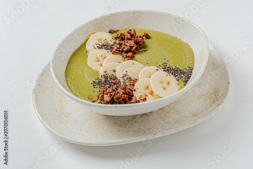 Delicious green smoothie bowl topped with fresh banana slices and crunchy granola
