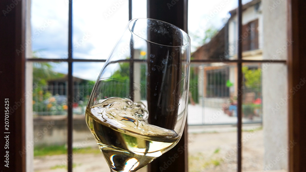 Fototapeta premium White Wine Swirling in Glass Before a Rustic Italian Window