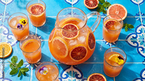 Refreshing citrus punch in a glass pitcher with garnishes on a vibrant tiled background