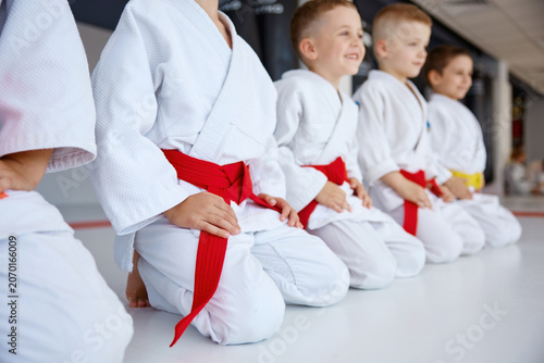 Cacausian children are kneeling respectfully in calm dojo setting with focused expressions