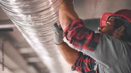 Worker installs ducting in commercial building with safety gear during daytime work