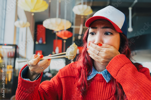 Vászonkép Young woman covering mouth, looking disgusted with dumpling on chopsticks