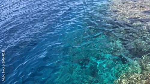 Clear blue water reveals a vibrant coral reef beneath the surface, showcasing marine life and underwater textures.