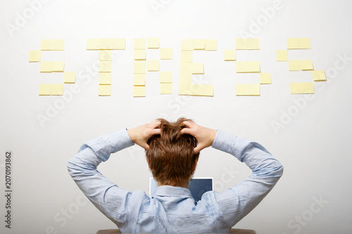 Stress and work pressure concept. Frustrated office worker sitting at a desk with hands on the head while looking at the word 