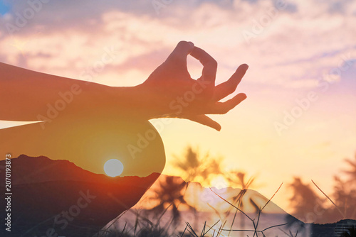 Meditation and mindfulness concept. Silhouette of a person practicing yoga in a lotus pose with a meditation hand gesture during a colorful sunset.  