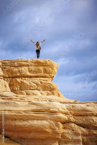 Freedom and inspiration concept. A man stands on a mountaintop with his arms raised against a blue sky.