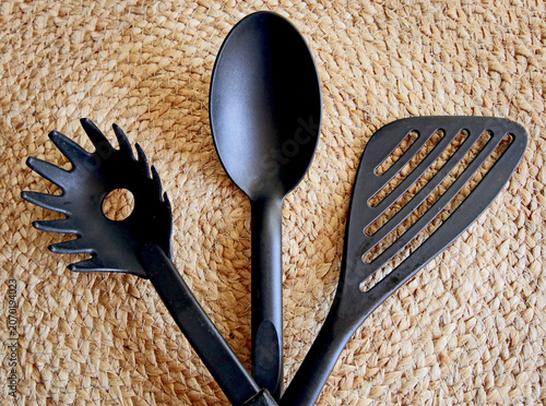 Kitchenware: black plastic ladle for soup and sauce, fork to serve spaghetti and kitchen spatula,  on natural background