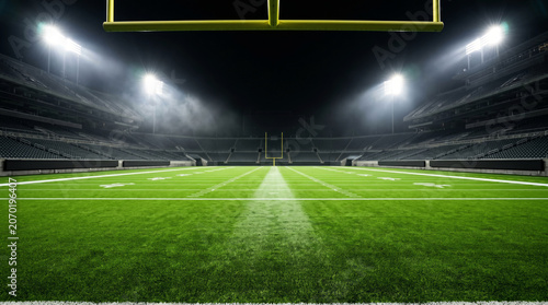 An empty American football stadium at night from inside the end zone looking the full length of the field, the turf blazing vivid green under four massive floodlight towers. Sports stadium empty arena