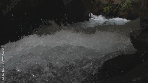 View on fast moving stream of mountain river. Powerful flood broking against stony surface splashing crystal clear water. Cool refreshing creek running in rocky terrain. Slow motion Close up