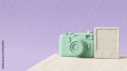 A minimalist mint green camera sculpture sits next to a blank white instant photo frame