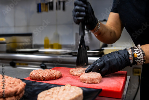 Chef pressing raw burger patties on a cutting board in a professional kitchen