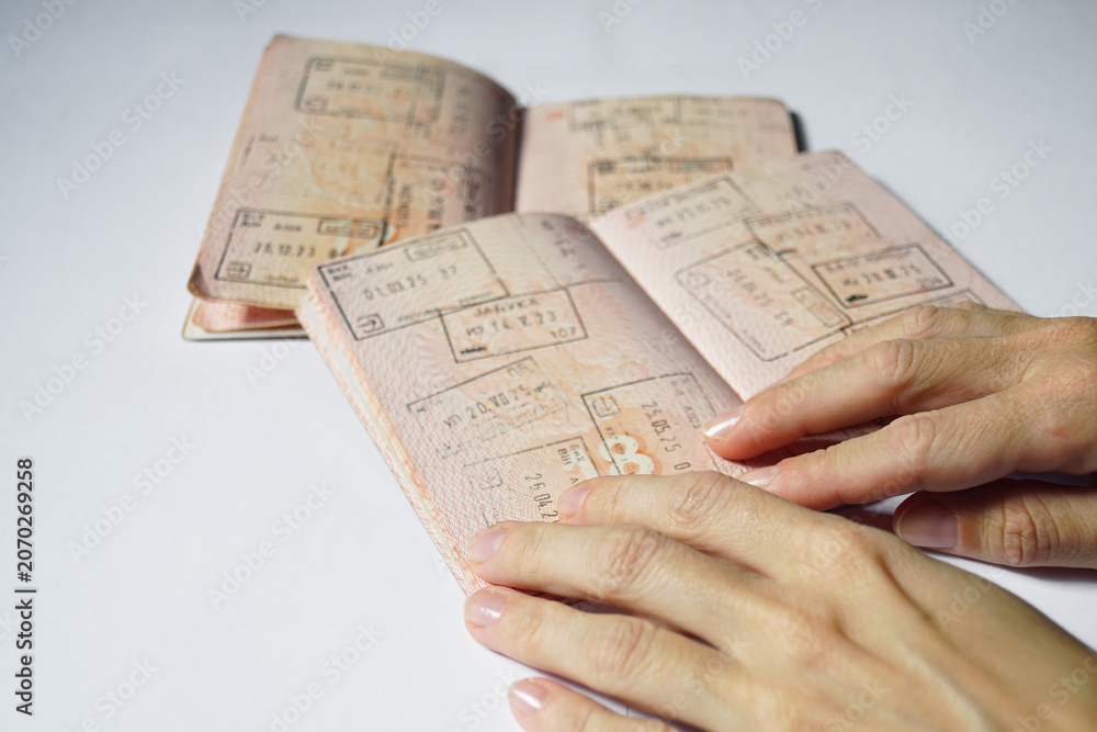 Fototapeta premium Close-up of hands holding passport pages filled with dated entry stamps from international journeys. Depicts travel verification, immigration record checking, and international mobility documentation.