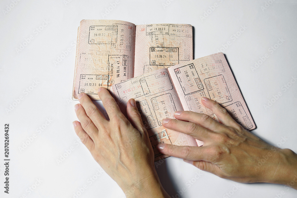 Fototapeta premium Female hands arranging several passports marked by years of international border crossings and regional travel. Symbolizes freedom of movement, interconnected destinations, and well-traveled lifestyle