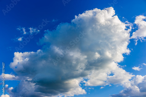 Fluffy white cumulonimbus cloud floating across a bright vibrant azure sky, capturing the serene beauty of a sunny day with distinct cottony textures drifting in the vast blue expanse