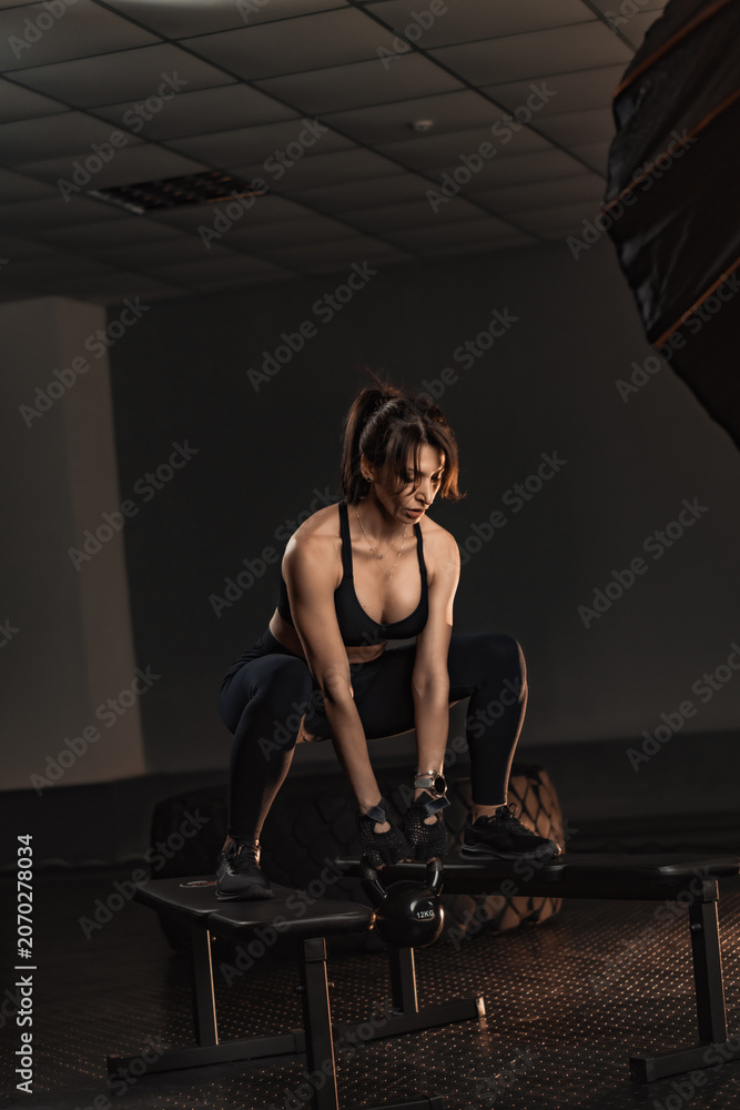 Naklejka premium Fit young woman trains with a kettlebell, showcasing power and endurance in a stylish fitness studio. The gym environment highlights her dedication to a healthy and active lifestyle