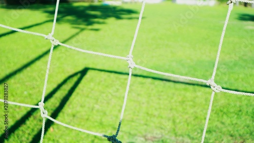 Close-up of a white soccer goal net on a lush green grass field with shadows