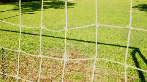 Close-up of a soccer net on a sunny green field with shadows