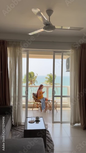 Interior living room writer caucasian woman sitting at balcony with notebook, warm light filtering through curtains, palm trees