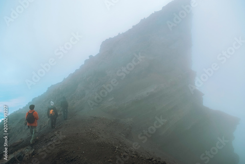 A Group of Hikers Standing on the Volcanic Rim above the clouds on a foggy day in the Alpine Desert Zone of Mount Meru, Arusha National Park, Tanzania
