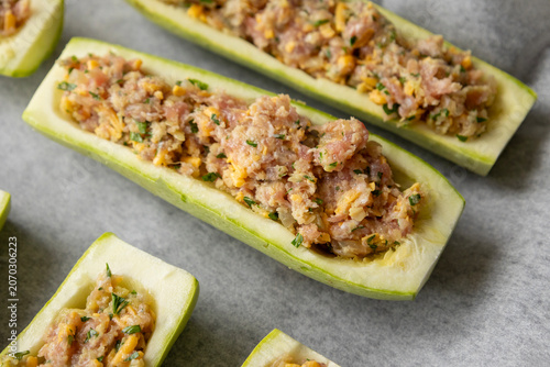raw stuffed zucchini boats packed with savory minced pork, topped with shredded cheddar cheese and fresh parsley in a baking tray
