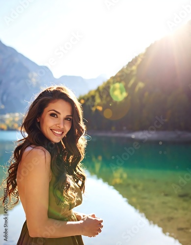 Smiling Young Woman Standing by Clear Mountain Lake in Sunny Alpine Landscape