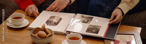 Fotografie Website header shot of middle aged adults turning photo album pages on table, sharing family memories and nostalgia, close up