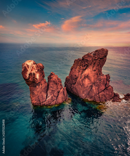 Fantastic morning view from flying drone of Red Rocks cliifs on Gli Scogli Rossi Faraglioni location. Spectacular summer sunrise on Sardinia island, Italy, Europe. Beauty of nature concept background.