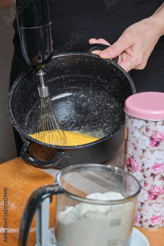 Eggs whipped vigorously. Whisking eggs in dark pot. Creating airy batter through focused mixing and steady grip