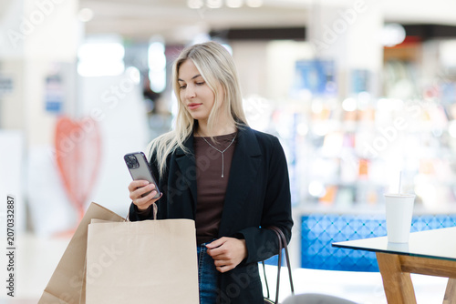 Woman holding smartphone and shopping bags in mall