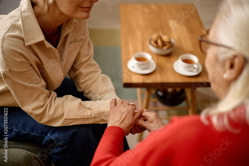 Bild auf Leinwand Middle aged Caucasian woman holding senior womans hands during supportive conversation at home, expressing care and trust