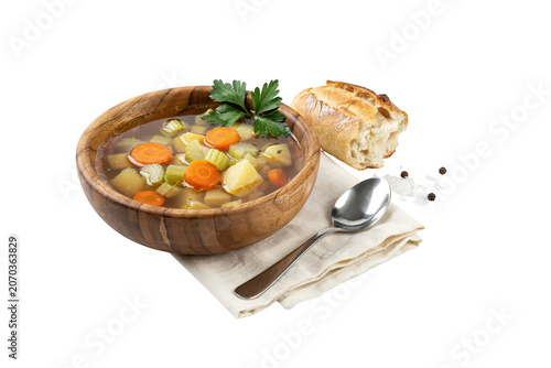 Wooden bowl of vegetable soup with carrots, potatoes, and celery, served with a piece of crusty bread on a napkin, isolated on black background