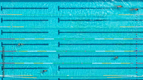 Schilderij op canvas Top down aerial view captures people swimming in a bright blue outdoor pool, featuring clear lane dividers, black lines at the bottom, and bright turquoise water under sunlight