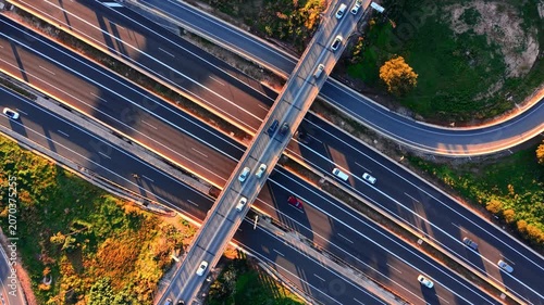 Highway intersection with crossing overpass and car, Spain. Aerial top-down view of multilane road, bridge structure, orange tree line and long shadow in warm light.