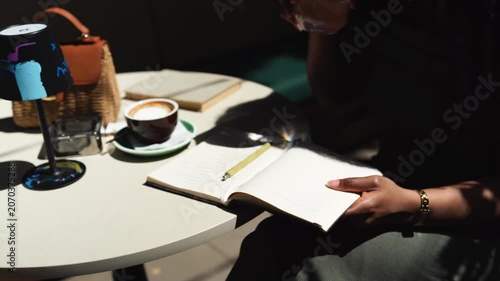 A black woman writes in a notebook paper diary closeup in a cafe on a sunny day outdoors